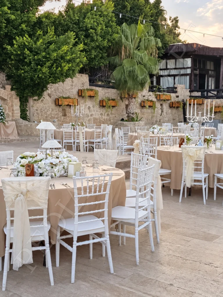 Pedias Concept Olympia Açık Alan’da taş duvarların önündeki beyaz sandalyeli yuvarlak masalar